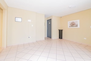 A spacious room with a tiled floor, a door, a small trash bin, and a framed picture on the wall.