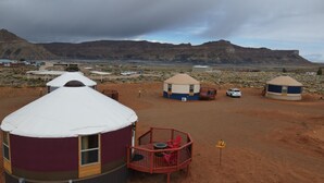 Una yurta con techo circular y una terraza de madera, rodeada por un paisaje desértico con montañas al fondo.