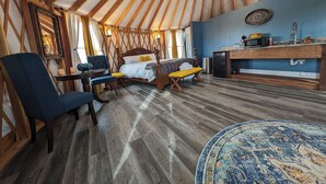 Una habitación acogedora con una cama, un escritorio y una silla. Cuenta con un ventilador de techo, una ventana con cortinas y una pared azul.