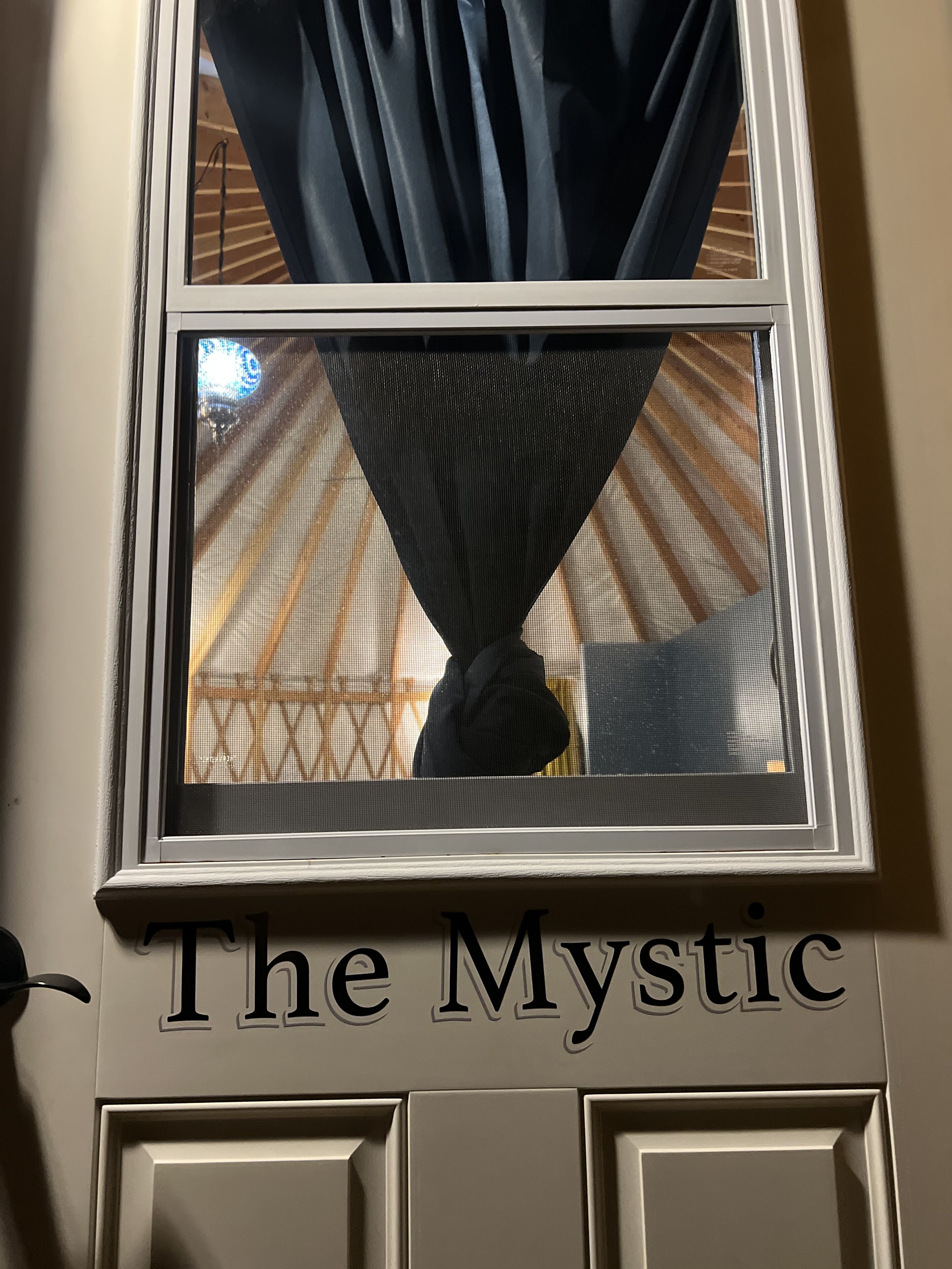 A window with a view of a building's interior, a black curtain, and the text "The Mystic" on the door below.