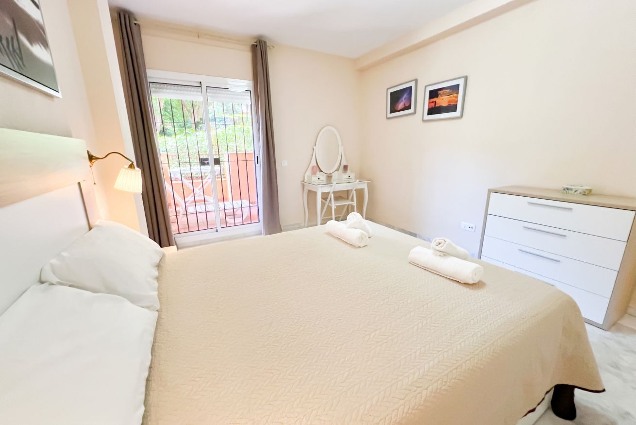 A hotel room with a bed, a desk, a chair, a mirror, and a window with curtains.