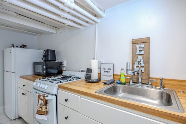 Una cocina con electrodomésticos blancos, encimera de madera y pileta de acero inoxidable, y un cartel que dice 'Follow Your Dreams'.