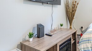 A modern room with a wooden TV stand, a mounted flat-screen TV, a small potted plant, and a built-in dishwasher. - Cozy 1-bedroom apartment located in UNBEATABLE location Washington DC (Washington)