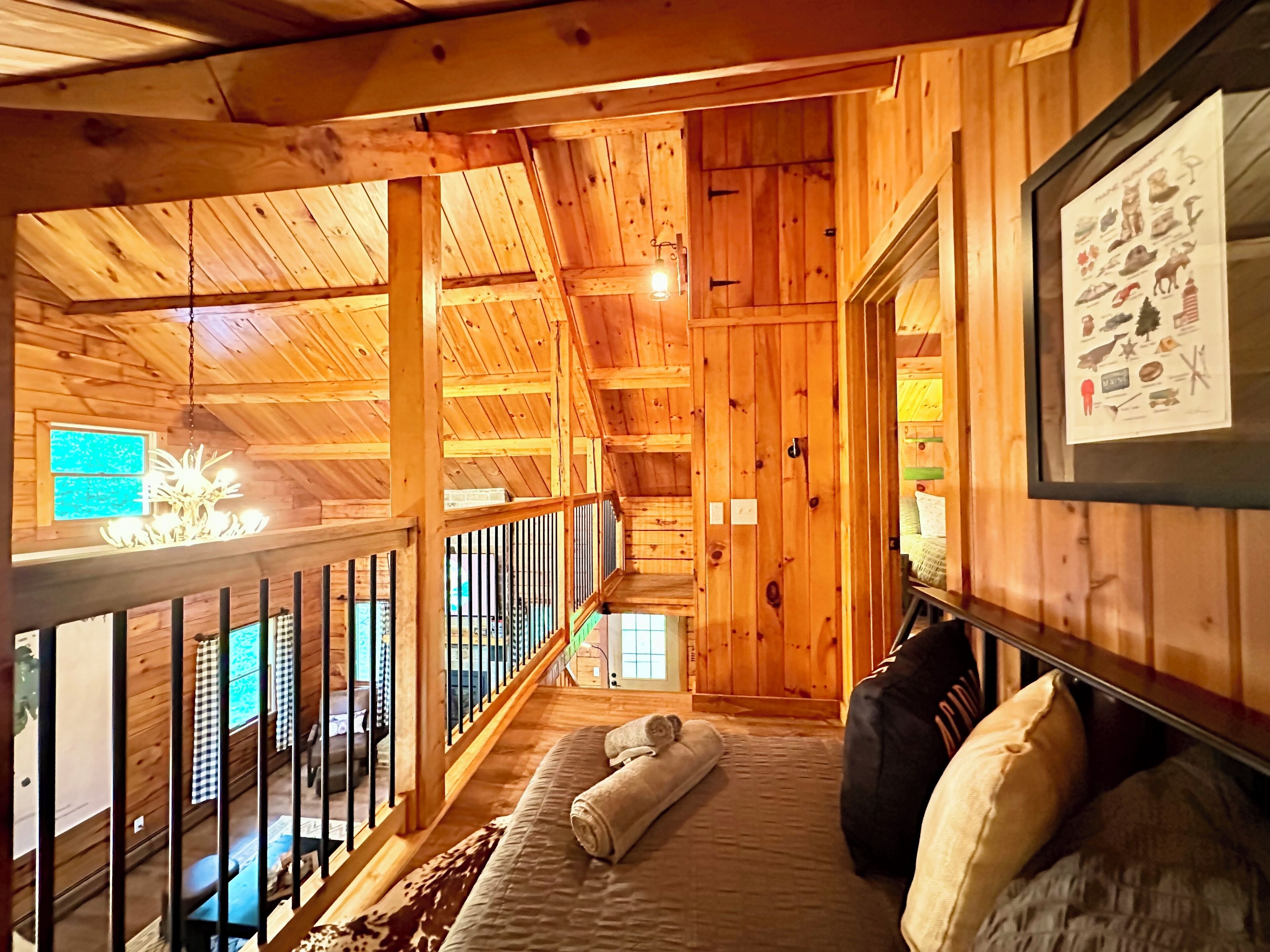 Interior de una cabaña de madera con balcón, una cama con almohadas y un cartel enmarcado en la pared.