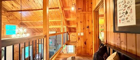 Interior de una cabaña de madera con balcón, una cama con almohadas y un cartel enmarcado en la pared.