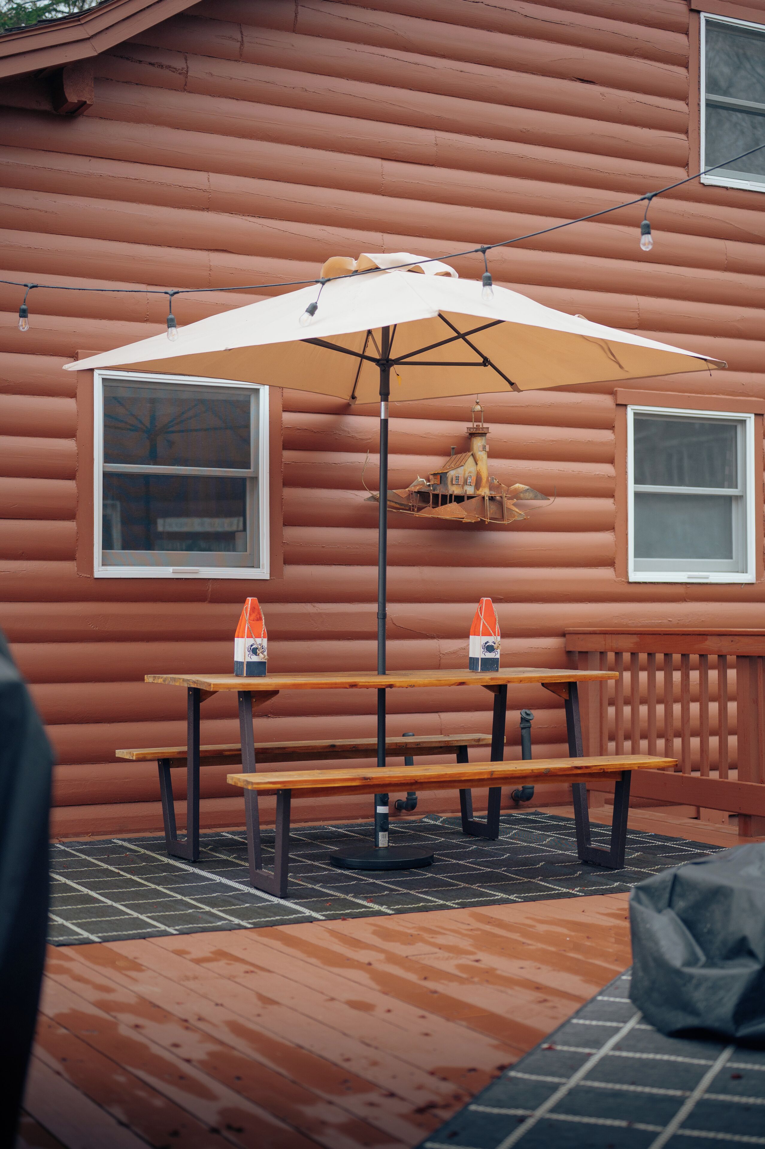 Eine Holzterrasse mit Picknicktisch und Sonnenschirm, eine Laterne sowie zwei Flaschen Orangensaft.