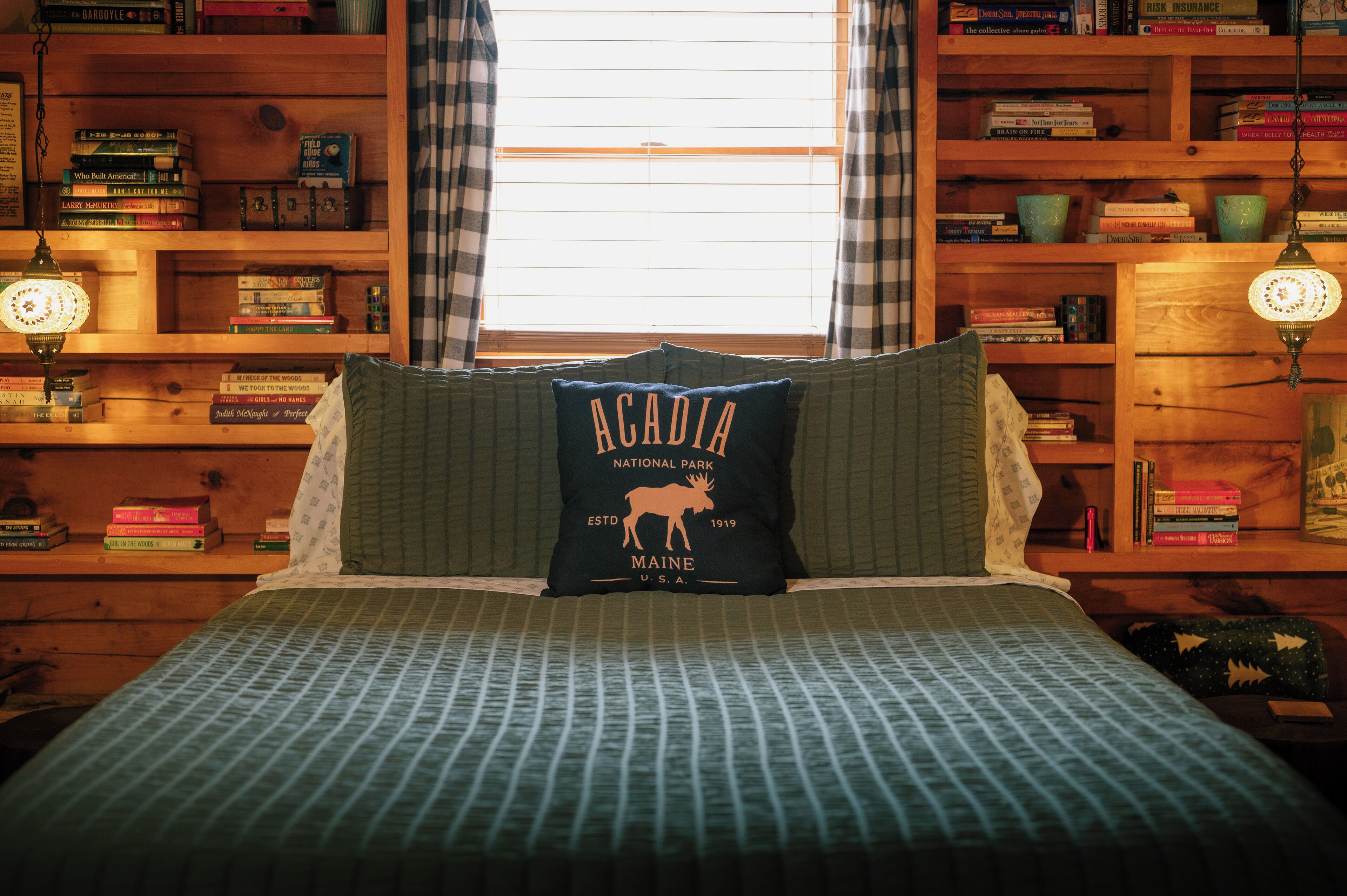Una habitación con una cama, un cojín con diseño de alce y estanterías de madera llenas de libros.
