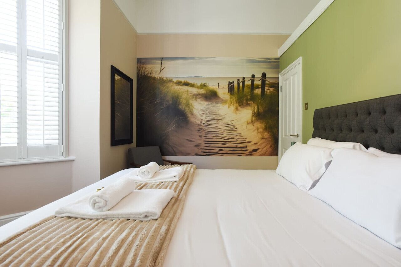 Una camera d'hotel con un letto, un grande affresco raffigurante una spiaggia sulla parete e una finestra con persiane.