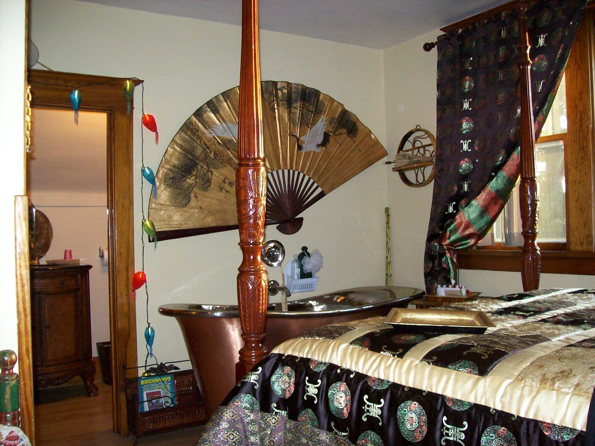A traditional bedroom with a four-poster bed, a fan, and a decorative wall hanging.
