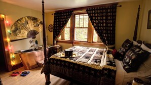 Un dormitorio tradicional con cama con dosel, suelo de madera, un ventanal con cortinas, una mesita de noche y una mesilla.