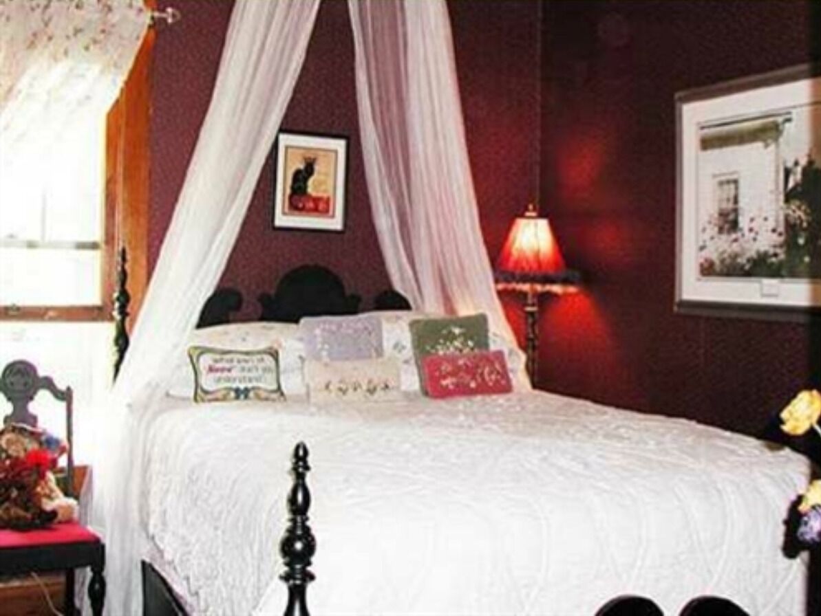 Une chambre à coucher avec un lit à baldaquin, une table de chevet, une lampe et un tableau encadré accroché au mur.