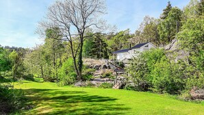 Une maison avec un escalier en pierre menant à un bâtiment blanc, entouré d’une végétation luxuriante et d’arbres.