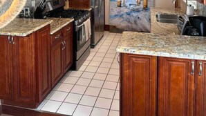 Una cocina con gabinetes de madera, electrodomésticos de acero inoxidable, encimeras de granito y piso de baldosas.