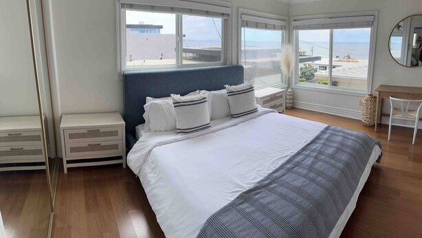 Un dormitorio con una cama grande, dos mesitas de noche, un aparador, una silla y vista a la playa.
