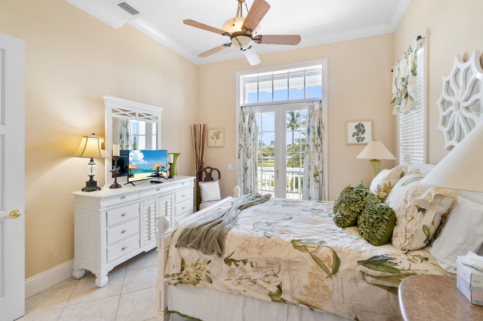 A bedroom with a bed, a dresser, a ceiling fan, a window with curtains, and a view of the outdoors.