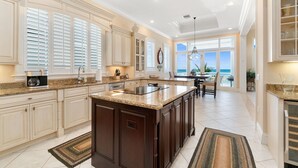 A spacious kitchen with a large island, white cabinetry, and a view to the outside. - Biltmore Beach House | Luxury 5-Br Beachfront Pool & Spa House | Sleeps 10 (Bonita Springs)