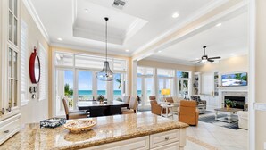 A spacious kitchen with a large island, a dining area with a view of the ocean, and a living room with a fireplace. - Biltmore Beach House | Luxury 5-Br Beachfront Pool & Spa House | Sleeps 10 (Bonita Springs)
