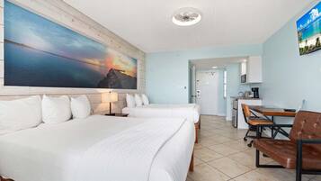 Une chambre d’hôtel avec deux lits, un bureau, une chaise et un grand tableau représentant un coucher de soleil sur l’océan.