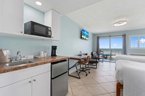 A modern kitchen with a microwave, sink, and coffee maker, leading to a balcony with a view of the beach. - Ocean View Hotel Room with Balcony- 2 Full Beds (Fort Pierce)