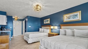 Habitación de hotel con dos camas, un escritorio con cafetera, una lámpara y obras de arte en las paredes.