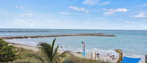 A beach with a clear sky, calm sea, and a rocky breakwater.