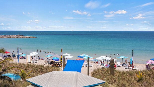 A beach with umbrellas and lounge chairs, a clear sky, and the ocean. - Ocean View Hotel Room with Balcony- King Bed #21 (Fort Pierce)