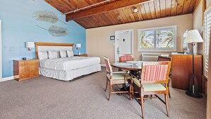 A bedroom with a bed, dresser, desk, and chair, a dining table with chairs, a ceiling fan, and a window with blinds. - Oceanfront Inn Suite, Ocean and Inlet Views, King Bed, #12 (Fort Pierce)