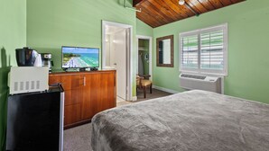 Une chambre à coucher avec un lit, un bureau avec un ordinateur, une chaise et une fenêtre avec des stores.