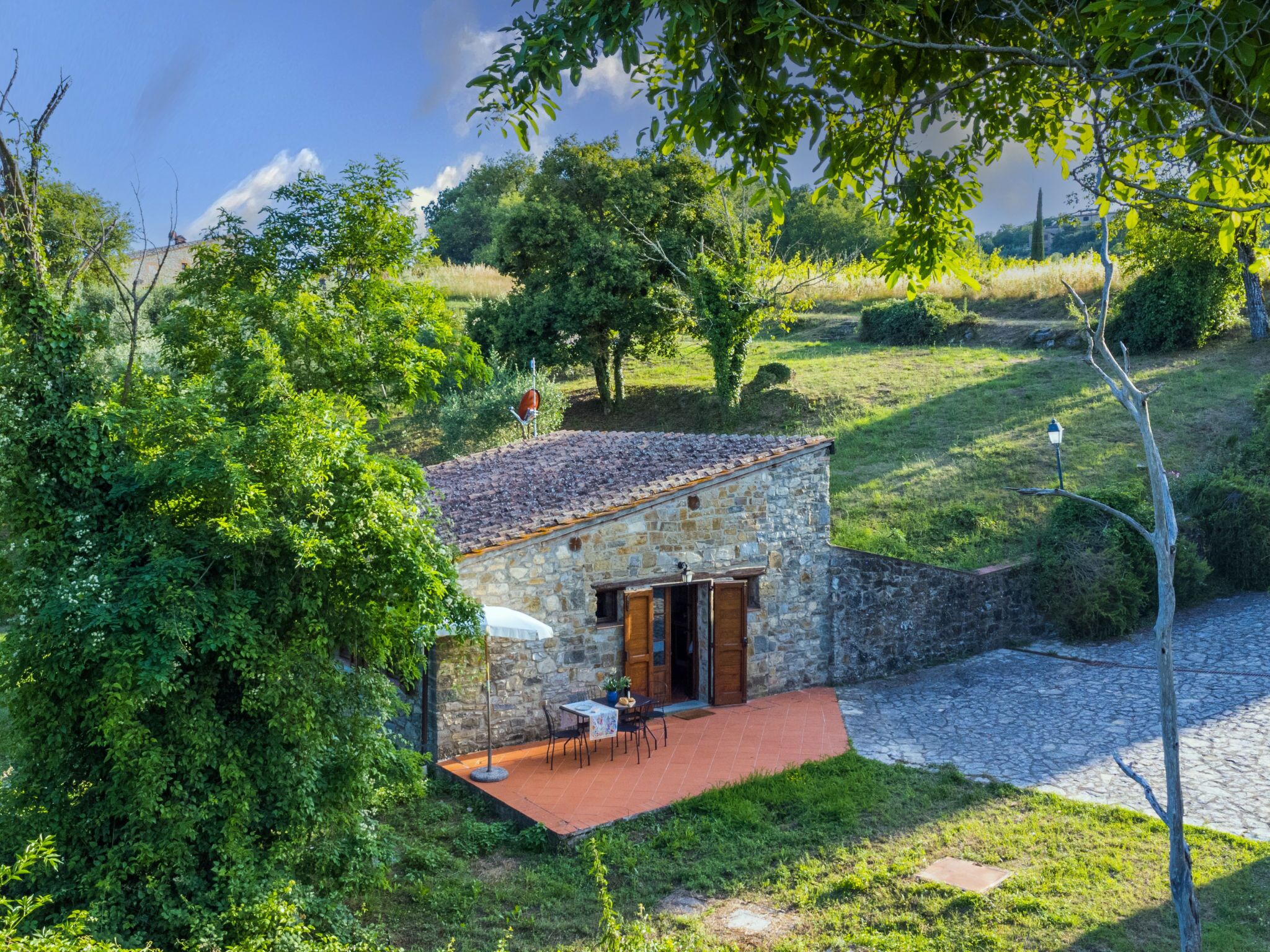 A stone building with a tiled roof, a wooden door, and a small patio with a table and chairs.