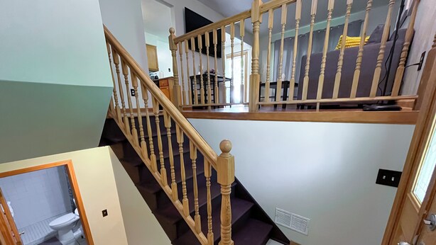 Un escalier avec des balustrades en bois et une petite plateforme recouverte d’une moquette sombre.