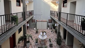 Un patio amplio con una fuente central, plantas en macetas y suelo de baldosas.