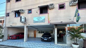 Un hotel con un letrero que dice "Pousada Golden House". Hay dos autos estacionados adelante y una bandera es visible en el edificio.