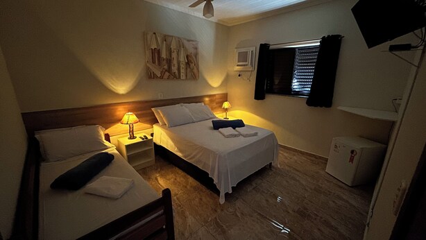 Habitación de hotel con dos camas, ventilador de techo, televisor y un refrigerador pequeño.