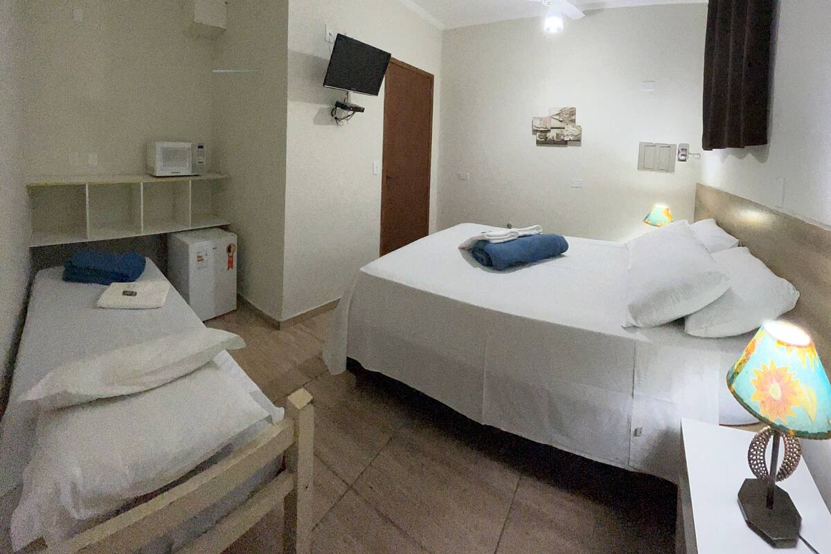 Habitación de hotel con una cama, un escritorio con lámpara, un televisor montado en la pared y un refrigerador pequeño.