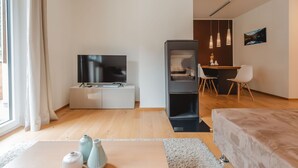 Una sala de estar moderna con un televisor de pantalla plana, un mueble multimedia oscuro, un comedor con mesa y sillas, y un ventanal con cortinas.
