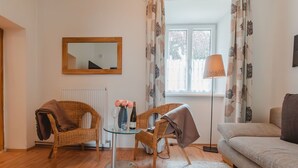 Een woonkamer met rieten stoelen, een glazen tafel met een vaas en een fles wijn, een bank en een vloerlamp.