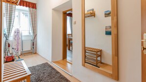 Een kamer met een grote spiegel, een houten bankje, een stofzuiger en een raam met gordijnen.