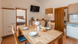 Een kleine keuken met houten kastjes, een eettafel gedekt met borden, glazen en een schaal fruit.