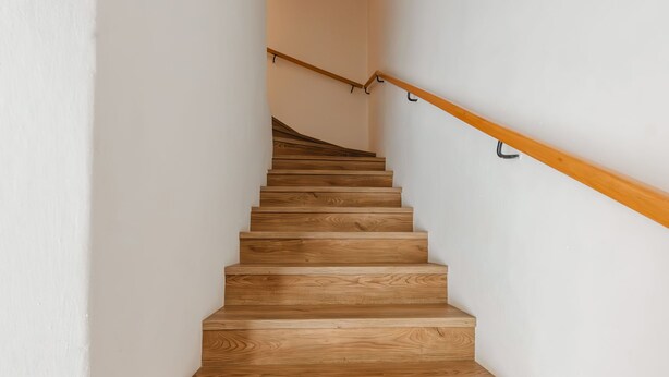 Een houten trap met houten leuning en witte wanden.