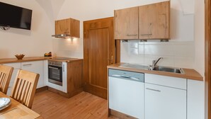 Een compacte keuken met houten kastjes, een ingebouwde oven, een vaatwasser en een televisie aan de wand.