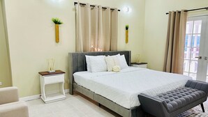 Un dormitorio con cama, mesitas de noche, un banco y cortinas.