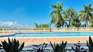Una piscina con borde de baldosas, rodeada de palmeras y una barandilla blanca.