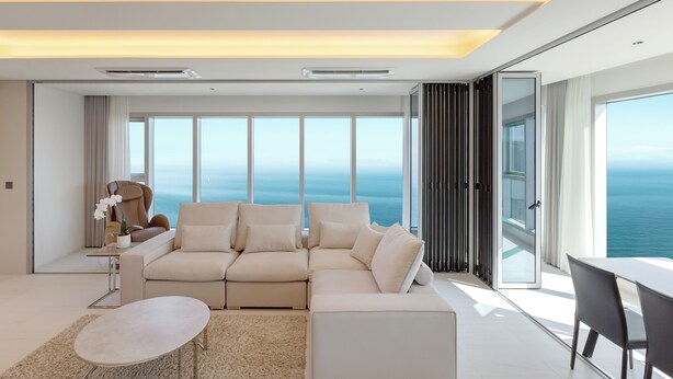 A modern living room with a sectional sofa, a dining table, and a view of the ocean. - NewCZ Haeundae Residence (Busan)
