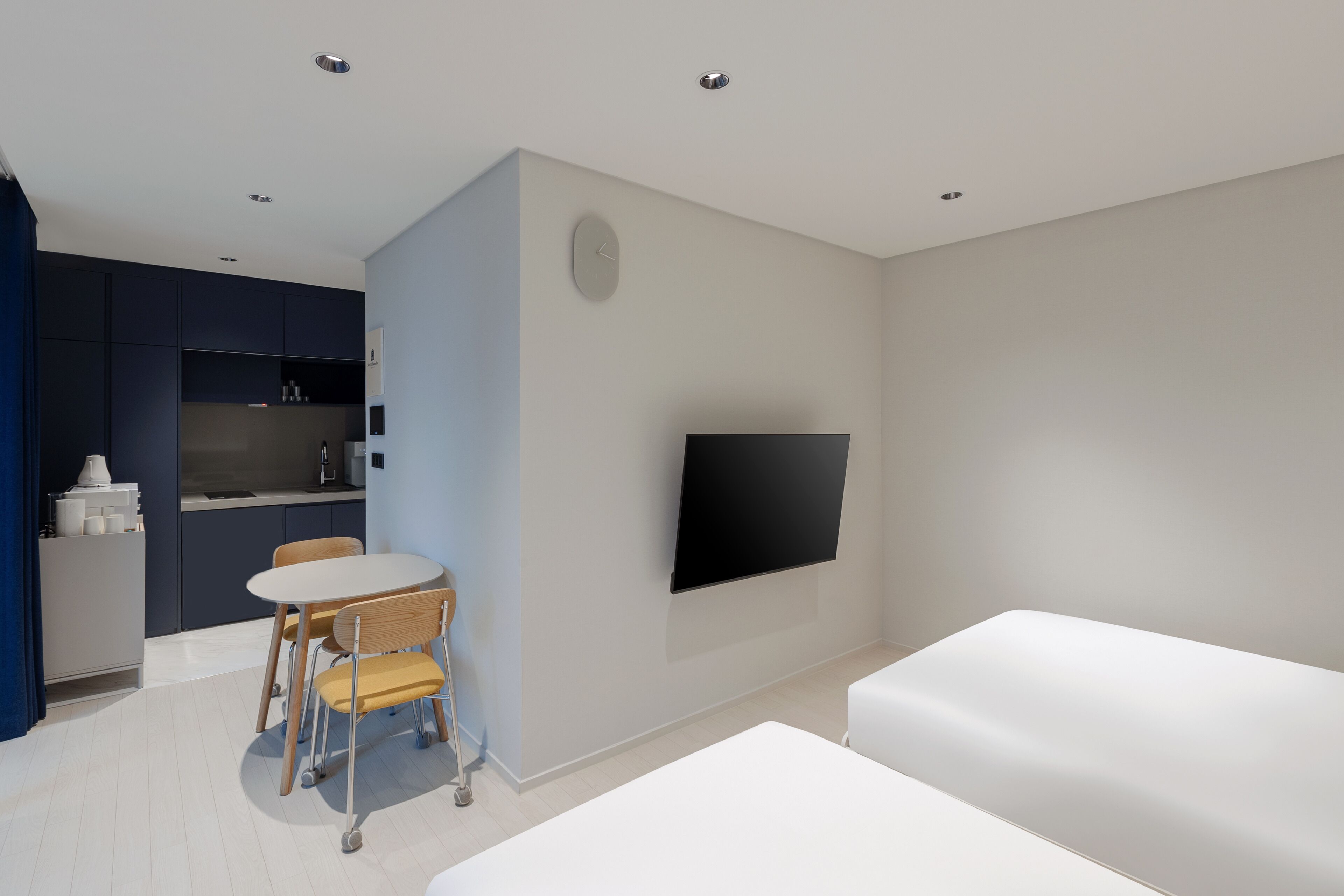 Un espacio habitable moderno y compacto con kitchenette, un televisor de pantalla plana montado en la pared, una zona de comedor con mesa y sillas, y una cama grande.