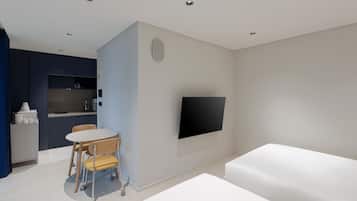 A modern, compact living space with a kitchenette, a flat-screen TV mounted on the wall, a dining area with a table and chairs, and a large bed.