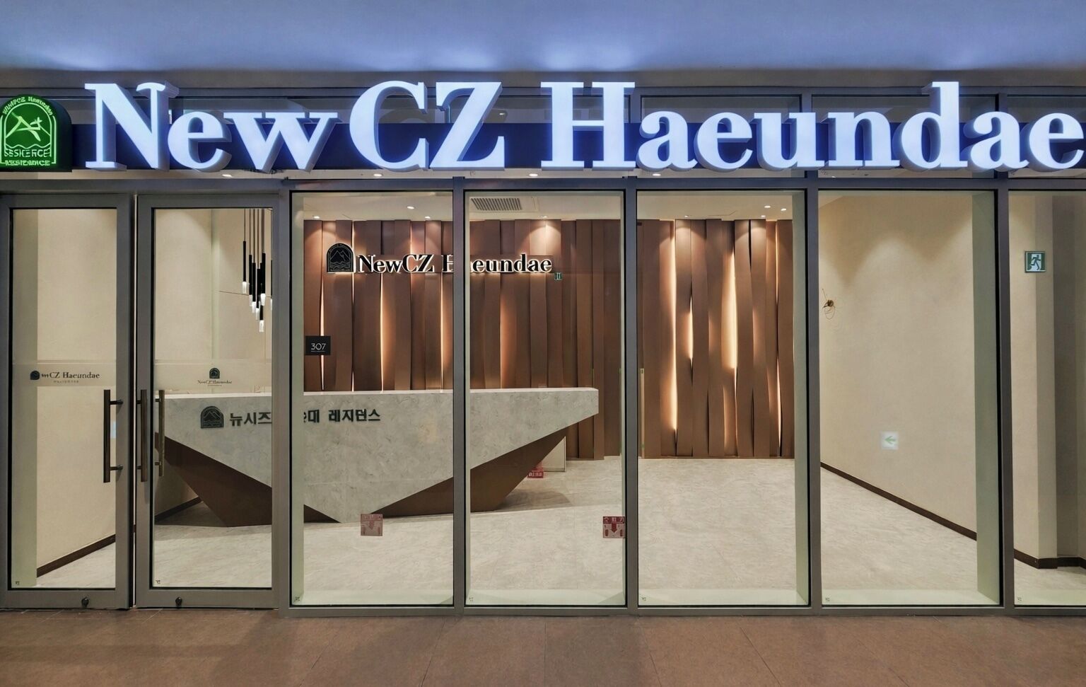 Entrada de hotel con fachada de vidrio, una recepción y un letrero que dice 'NewCZ Haendae'.