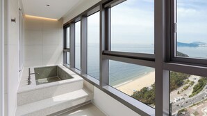 A high-rise hotel room with a large window overlooking a beach and cityscape. - NewCZ Haeundae Residence (Busan)