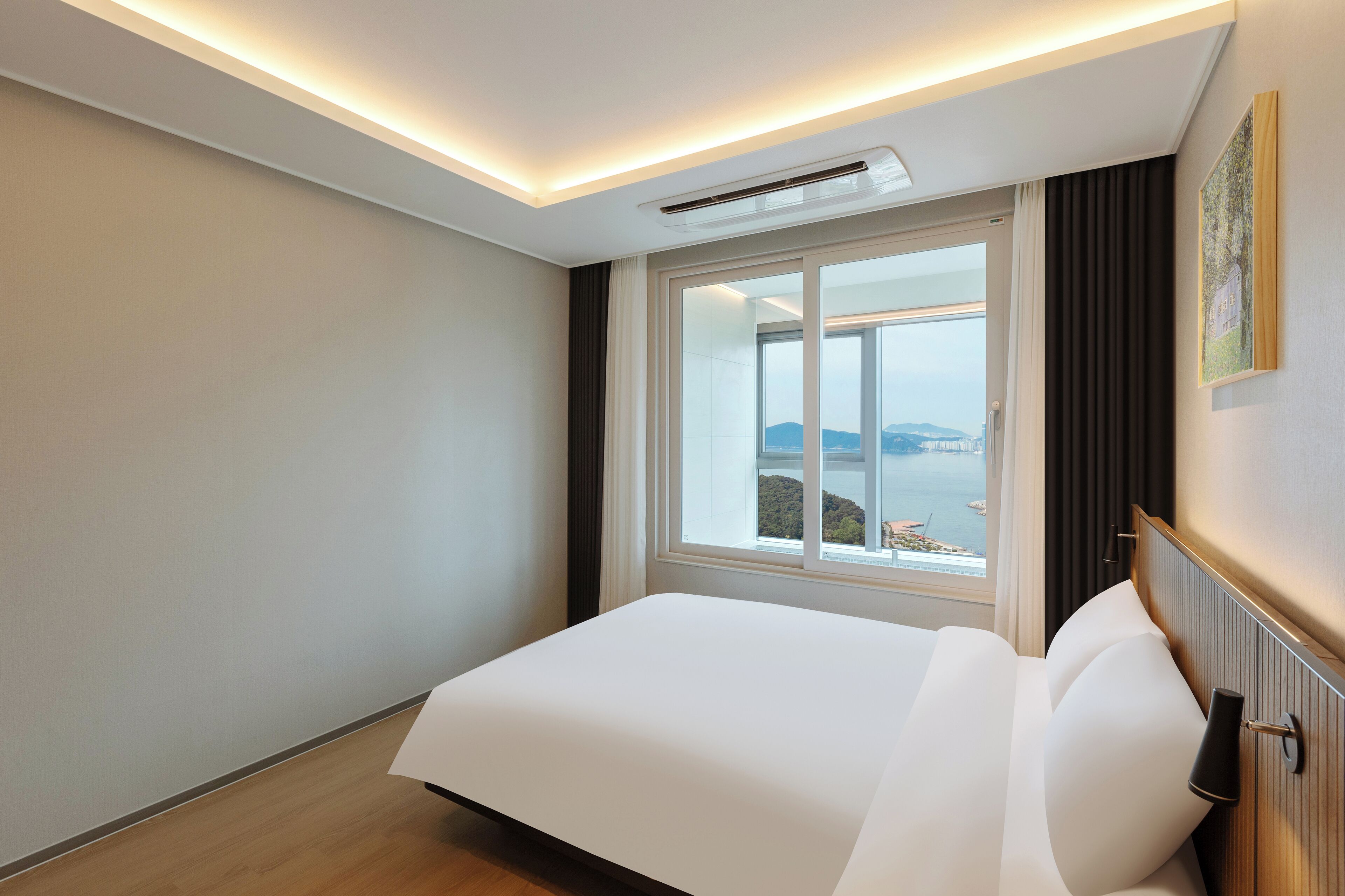 A hotel room with a large bed, a window with a view of the sea, and a ceiling light fixture.