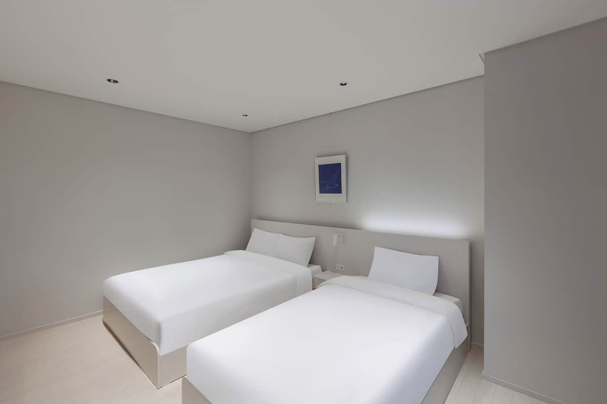 A modern hotel room with two single beds, a small bedside table, and a framed picture on the wall.