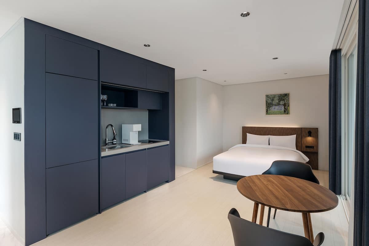 A modern hotel room with a bed, a desk, and a dining area.